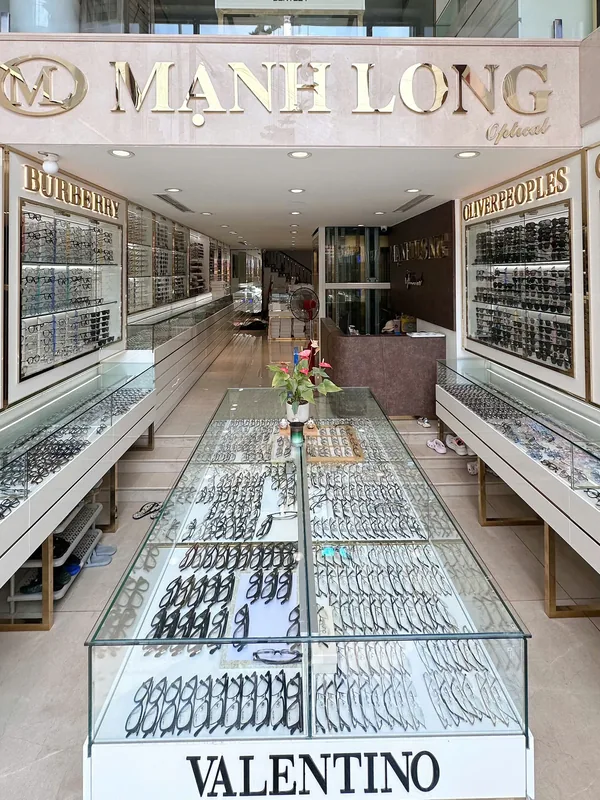 The frame tables inside Manh Long Optical at 147A Le Duan, Hanoi, with hundreds of frames laid out under glass and along both walls