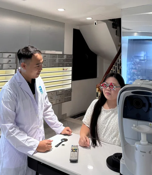 An eye test in progress in the testing room at Manh Long Optical, with a trial frame and an autorefractor